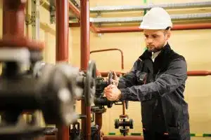 worker with protective helmet turns valve on industrial refinery oil pipes