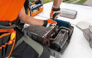 A technician adjusts components of a rooftop RV Camper HVAC unit, using tools from an open toolbox, while working on a building.