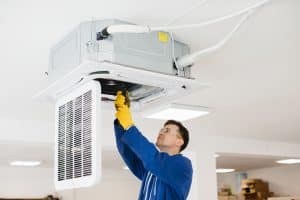 Hvac technician wearing safety glasses and gloves installing an air conditioning unit on the ceiling of a building