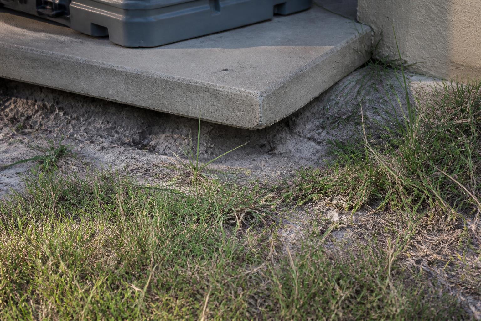 Outdoor AC condenser unit visibly tilted on a sunken concrete pad beside a Florida house