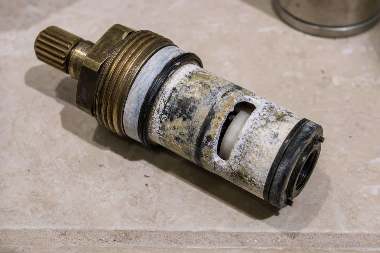 Worn shower valve cartridge showing mineral scale deposits on the spool surface