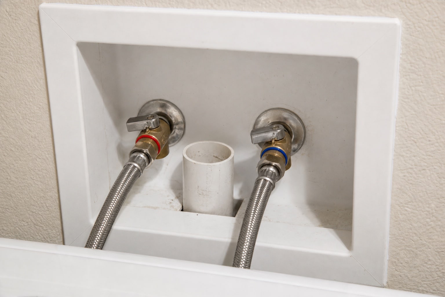 Braided stainless steel supply hoses connected to separate hot and cold quarter-turn valves in a laundry box