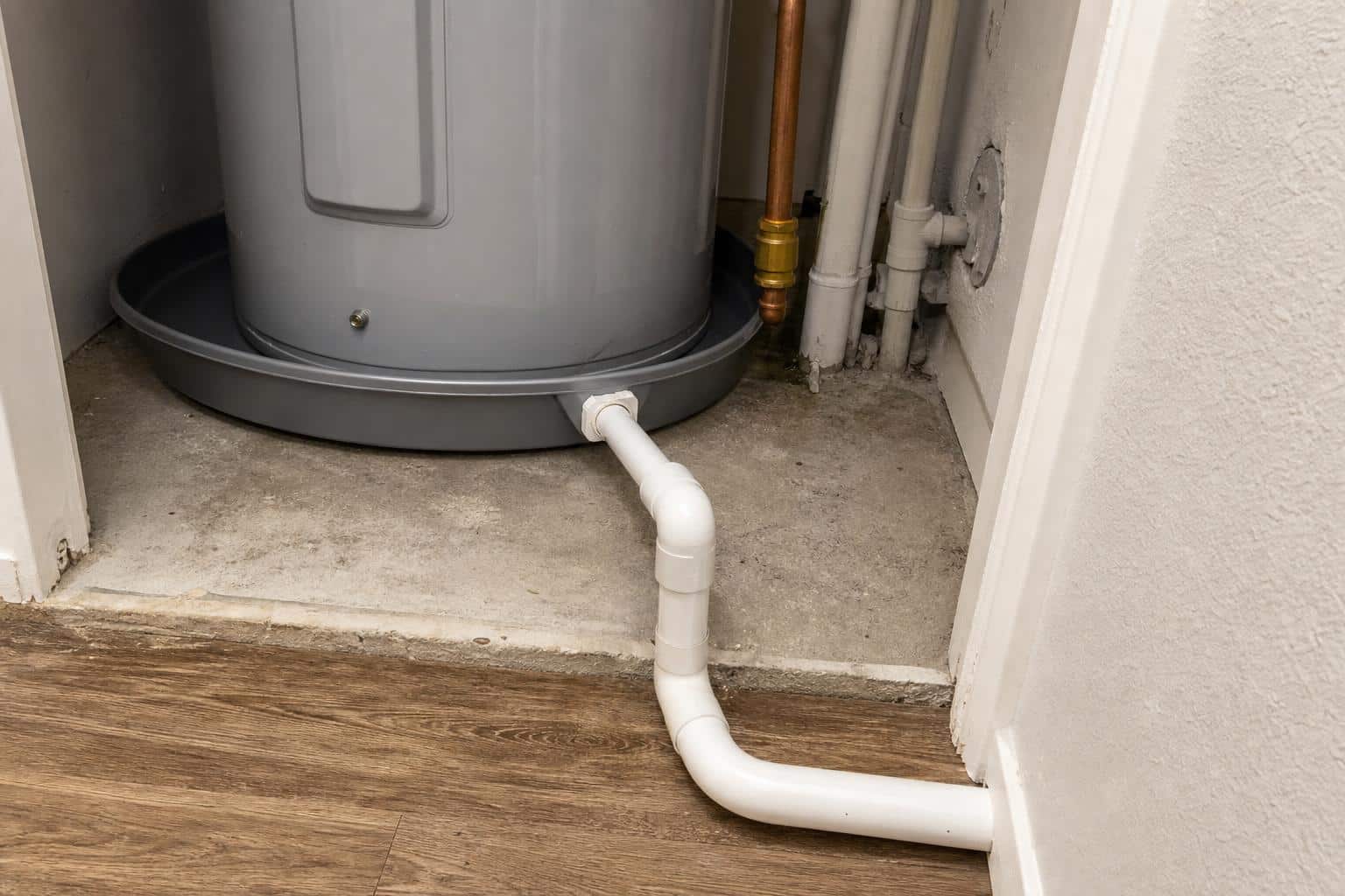 Water heater drain pan with connected PVC drain line in a residential utility closet