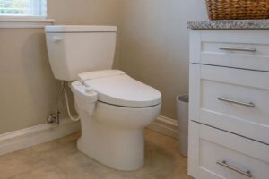 A modern Florida bathroom with a white elongated toilet fitted with a sleek bidet attachment and visible supply line connection, clean tile flooring, soft natural daylight from a nearby window, no.