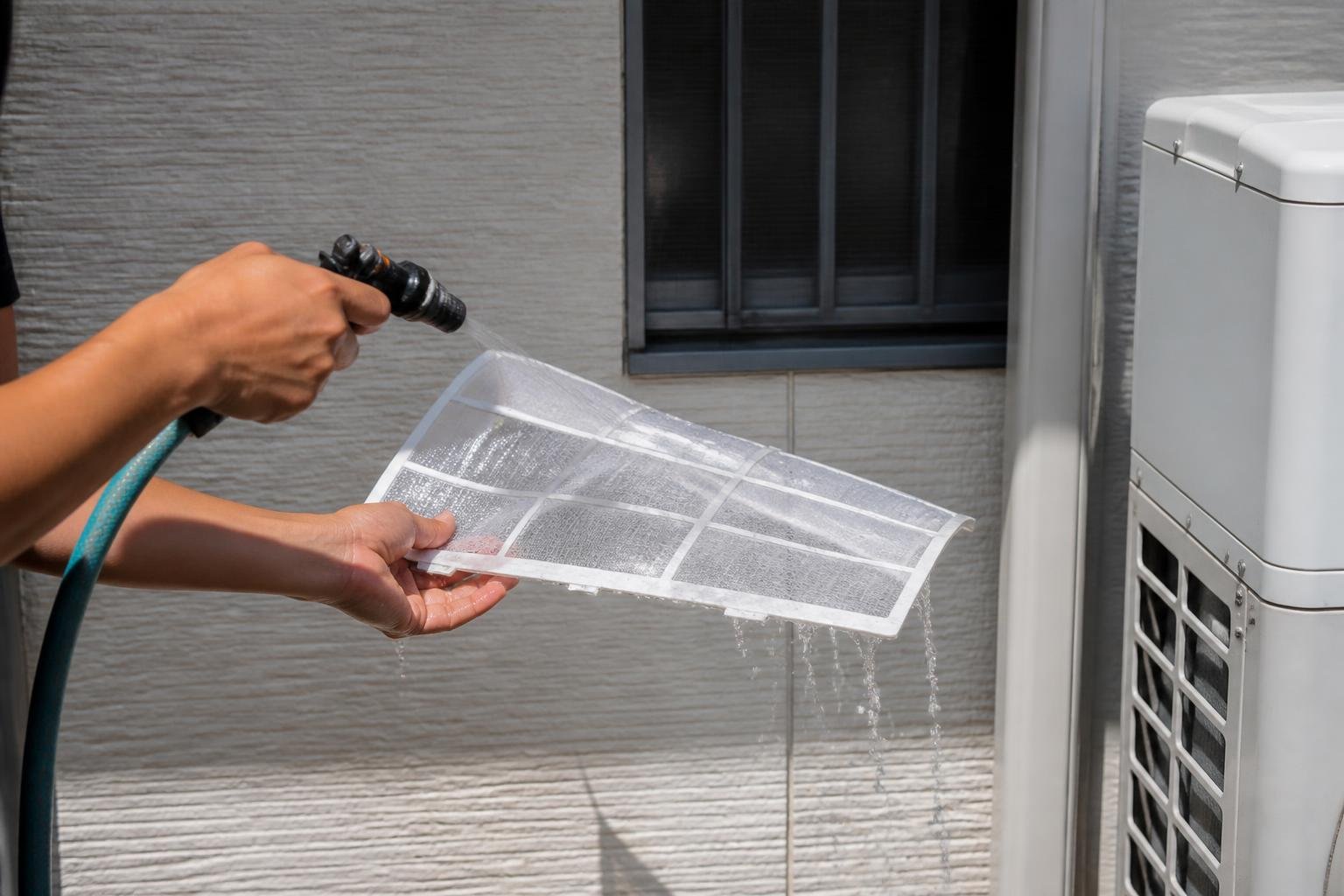 Close-up of a technician's hands rinsing a washable mini-split filter under water outdoors, natural daylight, no readable text, no brand logos, no people's faces
